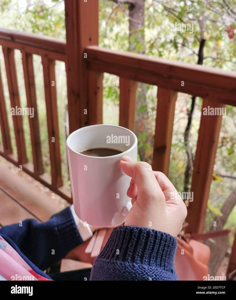 girl-hands-holding-a-coffee-mug-on-a-wooden-house-balcony-at-country-forest-resort-2ED7TCF.jpg